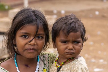 Angadihalli, Karnataka, Hindistan - 2 Kasım 2013: Genç kız küçük kız bebek kardeşi onun koluna taşıyan çift yüzlü closeup. Her ikisi de siyah saçlı bej renkli arka plan ile.