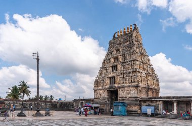 Belur, Karnataka, Hindistan - 2 Kasım 2013: Kahverengi taş Gopuram ana giriş, mavi gökyüzü Tapınağı içinde görüldü. Kabinleri, işaretler ve insanlar. Beyaz bulut karşı tören bayrak direği.