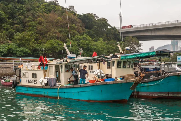 中国香港 2010年5月12日 港口小型渔船特写镜头 其他船只停泊在周围 两名男子正在准备船只 绿色植被和桥梁背景 — 图库照片