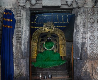 Belur, Karnataka, India - November 2, 2013: Chennakeshava Temple. Statue Devi Ranganayaki in Andal Shrine before Abisheka ceremony. Gray stone, golden arch and a black figure dressed in a dark green dress. clipart