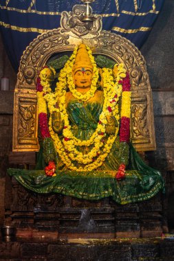 Belur, Karnataka, India - November 2, 2013: Chennakeshava Temple. Statue Devi Ranganayaki in Andal Shrine after Abisheka ceremony. Golden arch and a turmeric brown figure dressed in a dark wet green dress with yellow flower leis. clipart