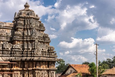 Belavadi, Karnataka, Hindistan - 2 Kasım 2013: Veera Narayana Tapınağı. En iyi kulenin birinde üç kahverengi taş Vimana cennet altında kompleks closeup. Komşu evler kırmızı çatılar.