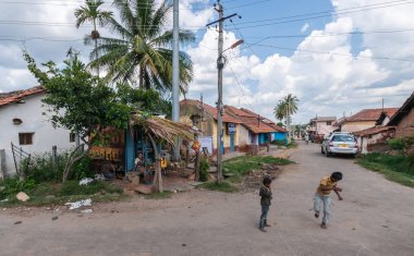 Belavadi, Karnataka, Hindistan - 2 Kasım 2013: Veera Narayana Tapınağı önünde sokakta iki küçük çocuğu oynamak. Kırmızı tavanlı evler, arabalar, ağır cennet ile mavi gökyüzünün altında. Dükkan sahibi kulübe arıyor.