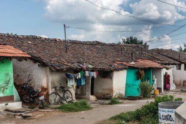 Belavadi, Karnataka, Hindistan - 2 Kasım 2013: Satır ile anne ve çocuk beyaz bulutlar ile mavi gökyüzü altında küçük konut Closeup. Renkli Çamaşırhane Kuru kilitleniyor. Yeşil otlar.