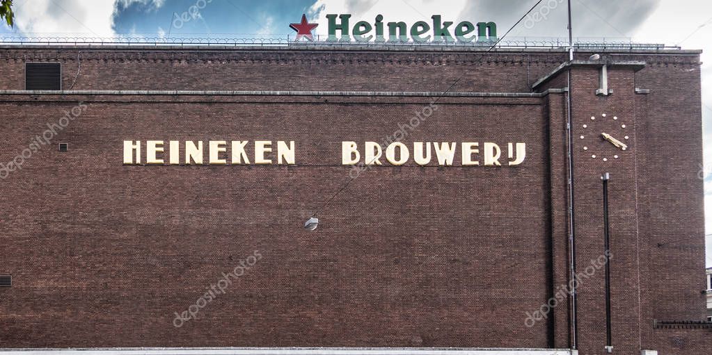 Amsterdam, the Netherlands - July 1, 2019: Brown brick side full wall of historic Heineken brewery along Stadhouderskade has name spelled out in beige.  Green Logo with red star, and clock.