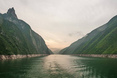 Wushan, Hubei, Çin - 7 Mayıs 2010: Wu Gorge, Yangtze Nehri. Yeşil suların üzerinde turuncu gökyüzü olan uzun bir manzara. Yeşil orman dağları ve uçurumlar tarafından yapılan kanyona..