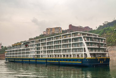 Wushan, Chongqing, Çin - 7 Mayıs 2010: Wu Gorge, Yangtze Nehri. Büyük otel nehir teknesi Victoria Cruises kıyı şeridi boyunca demirlemiş gümüş bulutların altında yüksek binalar var..