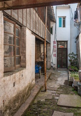 Tongli, Jangsu, Çin - 3 Mayıs 2010: Hutong dar geçitler, basit evler ve küçük işletmeler ağı. Kirli duvarların arasındaki sokak kahverengi kapıya çıkıyor. Bitkiler ve mavi üç tekerlekli bisiklet.