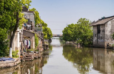 Tongli, Jlanangsu, Çin - 3 Mayıs 2010: Ana geniş kanal şehir merkezine yerleşim ve yeşil yapraklar ile girerken mavi gökyüzüne yansıyan kahverengi su. Çamaşır ekleme aksanları.
