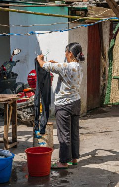Tongli, Jlanangsu, Çin - 3 Mayıs 2010: Kadın evin avlusunda ıslak pantolonunu kurutmak için asıyor. Scooter ve renkli kovalar yakında..