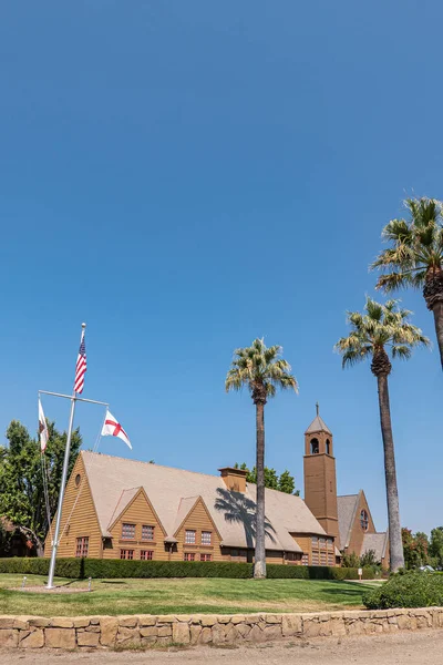 Los Olivos, California, ABD - 3 Eylül 2020: Vadi Kilisesi 'ndeki kahverengi ahşap St. Marks' ın portresi, mavi gökyüzünün altındaki yeşil parktaki çan kulesi. Öndeki bayrak direği..