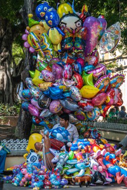Acapulco, Meksika - 25 Kasım 2008: Old Downtown. Erkek balon satıcısı büyük renkli balon kulesinin altında yeşil yapraklı büyük bir ağaçla oturuyor.. 