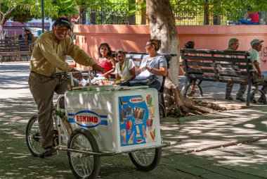 Leon, Nikaragua - 27 Kasım 2008: Eskimo markası satan üç tekerlekli dondurma satıcısı, parkta bankta oturan üç kadın. Yeşil yaprak.
