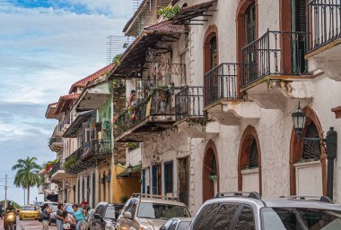 Panama City, Panama - 30 Kasım 2008: Mavi bulutların altındaki körfeze uzanan tarihi balkonlu evleri olan cadde. Arabalar ve insanlar. Biraz yeşil yaprak..