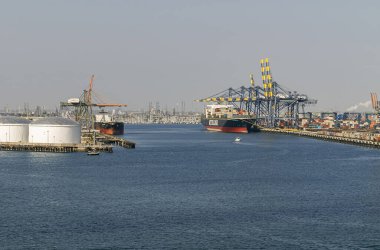 Los Angeles, ABD - 20 Nisan 2008 San Pedro Limanı. NYKLine siyah ve kırmızı konteynır gemisi Crades tarafından rıhtımda inceleniyor. Derin mavi su, açık mavi gökyüzü. Diğer gemi, beyaz tanklar ve binalar.