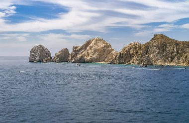 Cabo San Lucas, Meksika - 22 Nisan 2008: Baha California 'nın güney ucunda mavi bulutların altında gri bir okyanusta bej rengi kaya koleksiyonu. Minik kumsallar ve önünde küçük zevk gemileri..