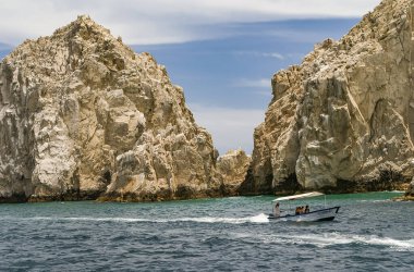 Cabo San Lucas, Meksika - 22 Nisan 2008: Baha California 'nın güney ucu. Mavi bulutların altında gri-yeşilimsi bir okyanusta birkaç bej kayaya yakın çekim. Küçük La Canela feribotu önde..