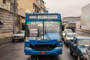 Quito, Ekvador - 2 Aralık 2008: Yağmurda araç ve kamyon trafiğinde sıkışan mavi özel kamu otobüsünün ön kısmı. Sarı binalar gri bulutların altında..