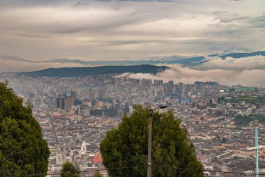 Quito, Ekvador - 2 Aralık 2008: Cerro El Panecillo 'dan aşağısı görüldü. Ufukta dağlar olan yoğun kahverengi ve beyaz bulutlar altında kuleleri ve düzenli konutları olan geniş şehir manzarası.