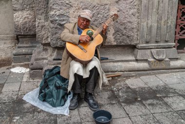 Quito, Ekvador - 2 Aralık 2008: Şehir merkezi tarihi. Son sınıf erkek gitaristin, gri taşa karşı sokakta oturması ve para için yalvarması.. 
