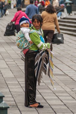 Quito, Ekvador - 2 Aralık 2008: Genç anne, satılık bilet sunarken sırtında asılı duran küçük çocukla konuşuyor. Arka tarafta yayalar olan sokak manzarası..