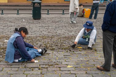 Quito, Ekvador - 2 Aralık 2008: Şehir merkezi tarihi. 2 kadın belediye çalışanı kare üzerinde sırtüstü oturmuş kaldırım taşlarının arasındaki otları elle temizliyorlar..