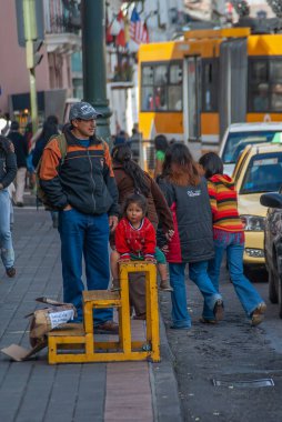 Quito, Ekvador - 2 Aralık 2008: Şehir merkezi tarihi. Mavi kotlu ve turuncu yelekli baba kırmızı gömlekli küçük kız otobüs durağında sarı ayakkabı cilası sandalyesinde oturuyor. Çevredeki insanlar.