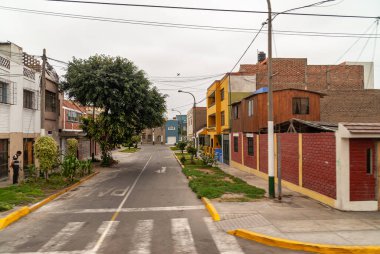 Lima, Peru - 4 Aralık 2008: Gümüş gökyüzü altında daha iyi bir muhitte yeşil ve ağaçlı boş caddede basit evler. Evler gri, mavi, sarı ve kırmızıya boyanmıştır.. 