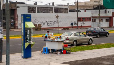 Lima, Peru - 4 Aralık 2008: Kadın satıcı sokak boyunca itme sepetinden kendi kendine sabah içkileri satıyor. Mavi Telefon kulübesi yakınlarda. Arkadaki beyaz fabrika duvarı..