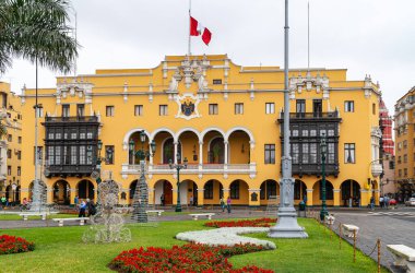 Lima, Peru - 4 Aralık 2008: Pancho Fierro Müzesi, Plaza de Armas 'ın yeşil çimlerinin ve çiçeklerinin arkasında, üzerinde gümüş gökyüzü altında kırmızı-beyaz Peru bayrağı bulunan sarı tarihi bina.