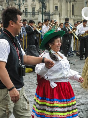 Lima, Peru - 4 Aralık 2008: Plaza de Armas. Dişi halk dansçısı turistleri eylem merkezine götürüyor. Arkadaki müzisyenler.