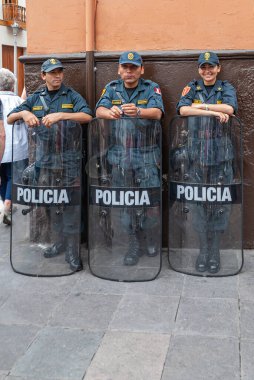 Lima, Peru - 4 Aralık 2008: Yeşil giysili 3 polis memuru, 1 kadın ve 2 erkek, kahverengi ve turuncu duvarların önünde birer ayaklanma kalkanı olarak duruyor.