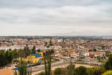 La Serena, Şili - 7 Aralık 2008: Beyaz bulutların altında okyanus ve dağlarla şehir merkezinin bir kısmına kuş bakışı görüş. Önünde yeşil yapraklar olan binaların derlemesi.