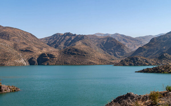 Vicuna, Chile - December 7, 2008: landscape of brown mountains and azure water Lake Embalse Puclaro in Andes along highway 41 under deep blue sky.