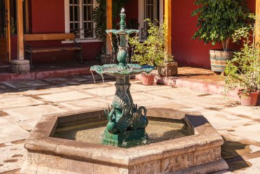 Vicuna, Şili - 7 Aralık 2008 Destileria Capel, Pisco dilstillery. Bahçenin ortasındaki küçük yeşil metal çeşmenin arkasında kestane rengi duvarlar var. Biraz yeşil yaprak..