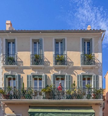 Saint Tropez, France - July 13, 2024: Downtown scenery. Facade above Dumas and Limbach art shop in Rue Louis Blanc. Green plants and cacti on balconies with 1 colorful statue of a woman
