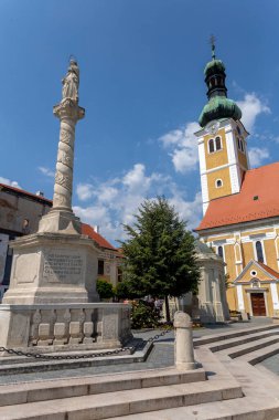 Macaristan 'ın Koszeg kentindeki Jurisics Meydanı' ndaki St. Imre Kilisesi 'nde bir yaz günü ön planda Maria sütunuyla.
