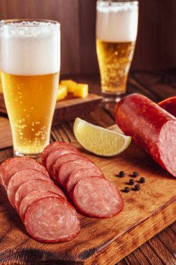 Kesme tahtasına dilimlenmiş füme salam. İki bardak bira, bir avuç peynir ve zeytin.