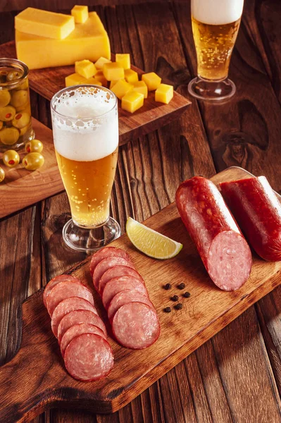 Kesme tahtasına dilimlenmiş füme salam. İki bardak bira, bir avuç peynir ve zeytin.