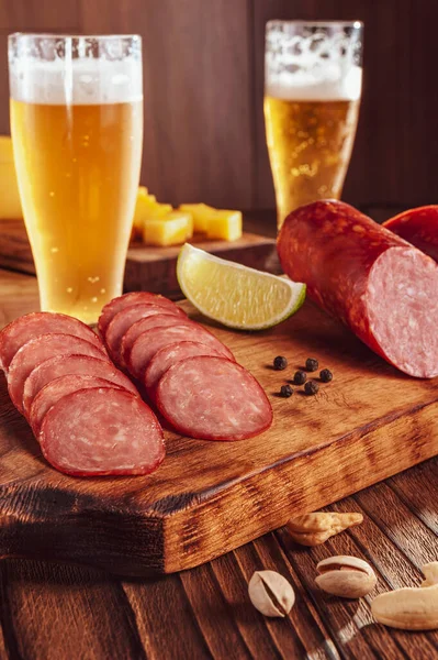 Kesme tahtasına dilimlenmiş füme salam, iki bardak bira, bir avuç peynir, zeytin ve şam fıstığı.