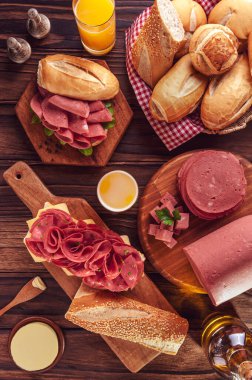 Mortadella sandwich with orange juice, bread, butter and spices on wood background - Top view clipart
