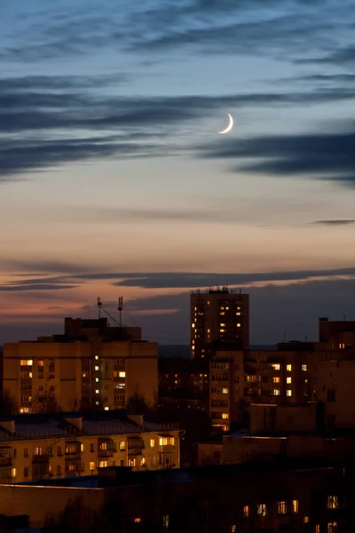 crescent moon over houses with illuminated windows