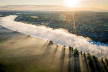 Sabahın erken saatlerinde. Sisli nehir. Nehir vadisi, sabah sisi, gün doğumunda. Yukarıdan bak. Güneş ışınları ağaçların üzerinden sisi delip geçiyor.