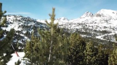 Dağlara ve kayak yamaçlarına bakan çam ağaçlarının yanından pürüzsüz bir yolculuk. Andorra 'daki Grandvalira kayak merkezi. Muhteşem karlı dağlar ve mavi gökyüzü.