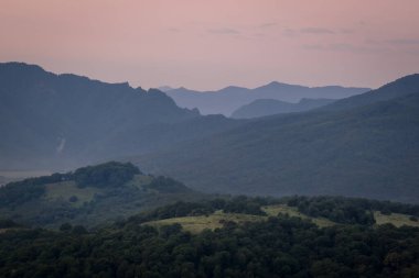 Şafak sökmeden bir saat önce. Sabah sisli dağların siluetleri, ön planda çimenler ve ağaçlar. Lagonaki Platosu, Adygea Cumhuriyeti, Rusya