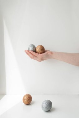 Güneş ışığında bir duvarın önünde altın ve gümüş Paskalya yumurtalarını tutan bir kadın.