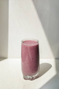 Blueberry pacific pink smoothie in a transparent glass on light background with long shadows, top view. Milk Shakes. Vitamin healthy food