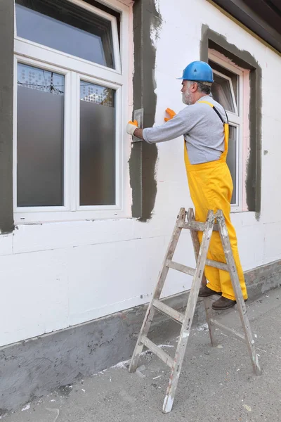 工人在聚苯乙烯泡沫塑料墙上用梯子涂布保温砂浆 — 图库照片