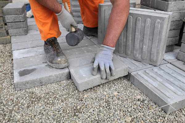 Construction site, worker installing concrete brick pavement, using hammer