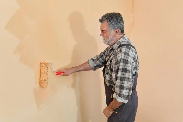 在房间里画墙的工人用漆辊涂上橙色的颜色 — 图库照片